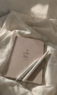 A soft pink notebook and pens resting on linen