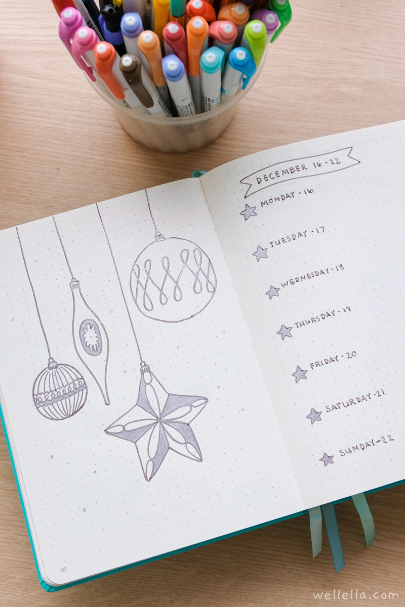 A teal notebook open to a weekly page decorated for Christmas with silver ornaments.