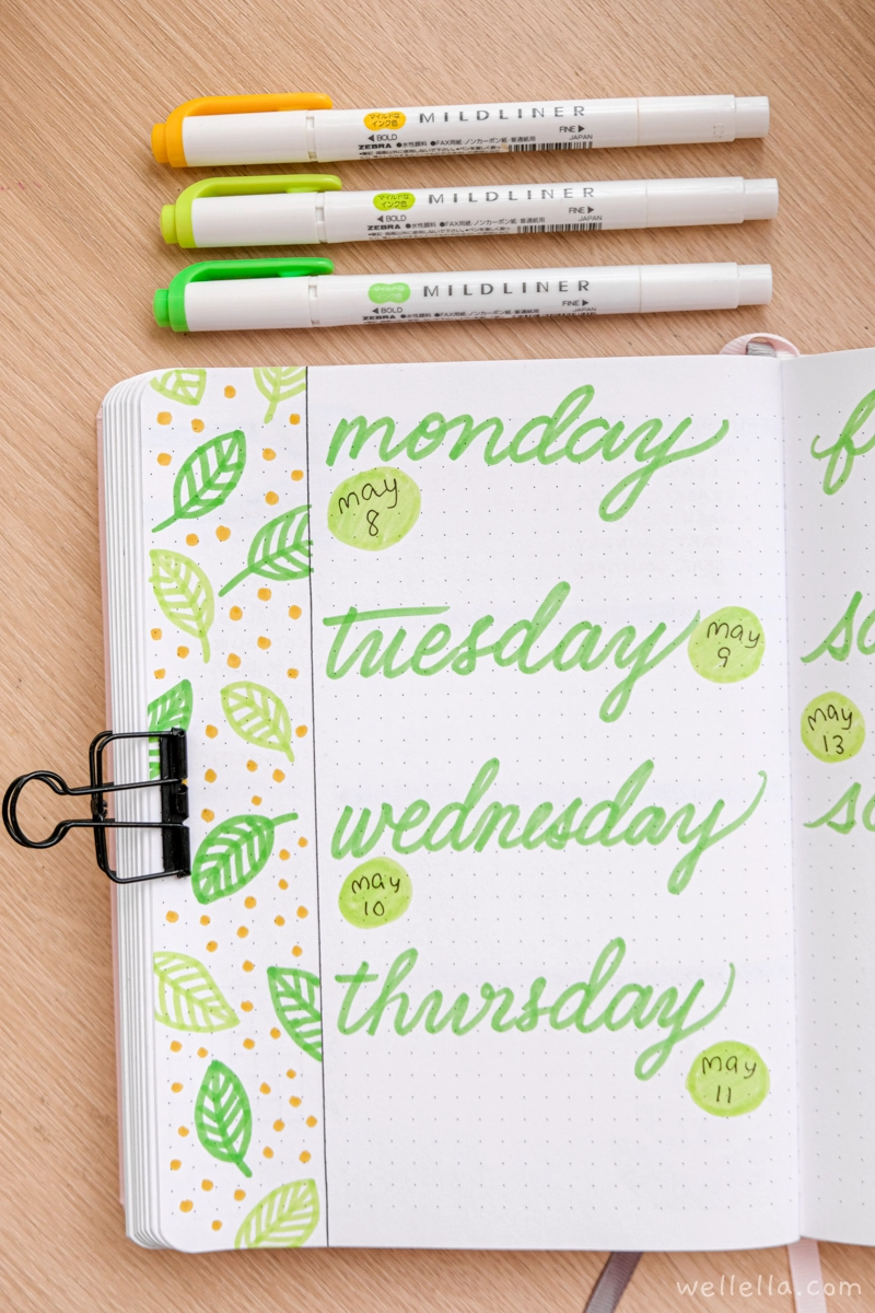 A bullet journal page decorated with green leaves drawn in markers. The days of the week are written in green marker in an oversized cursive.