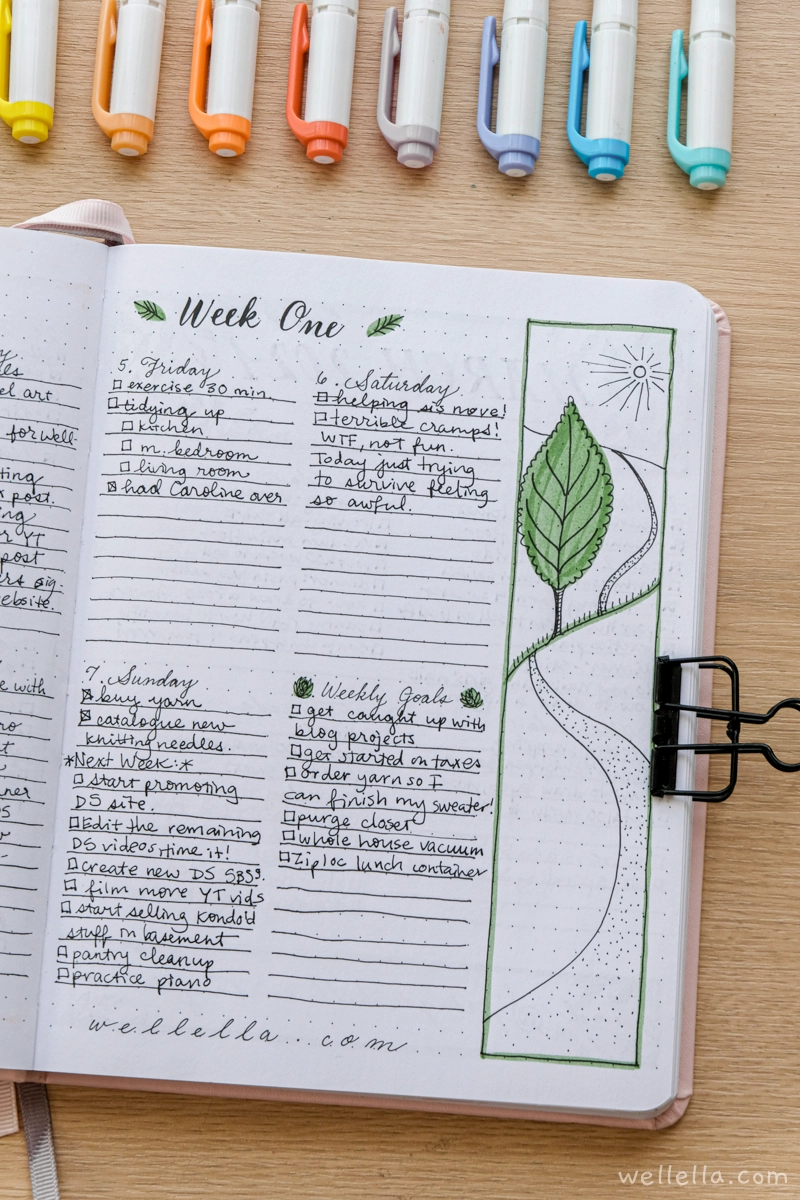 An open notebook with "week one" written at the top and notes for each day written in different sections. The side of the page features a drawing of a tree and a path.