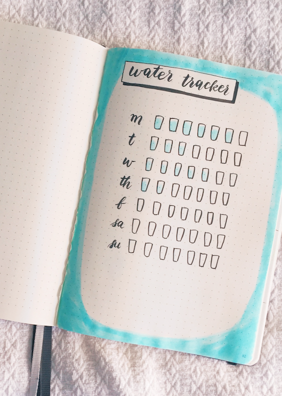 a dot grid notebook with a chart for tracking water consumption, showing doodles of cups colored blue.